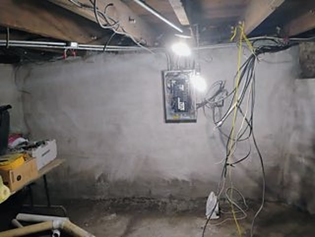 A basement with its old walls coated in gray cement, an electrical panel on the far wall