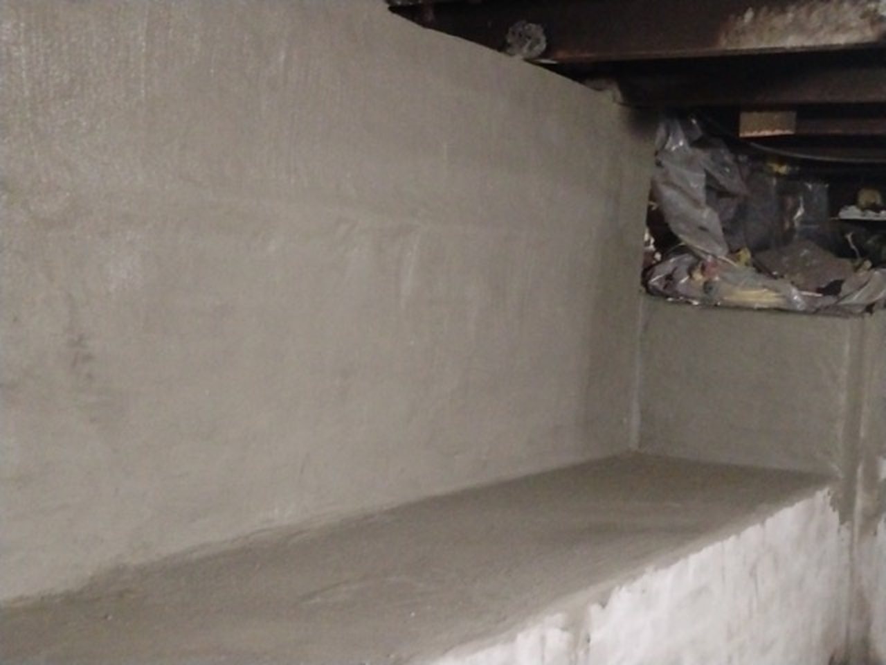 A basement wall coated in fresh cement, with a new concrete ledge poured along the bottom