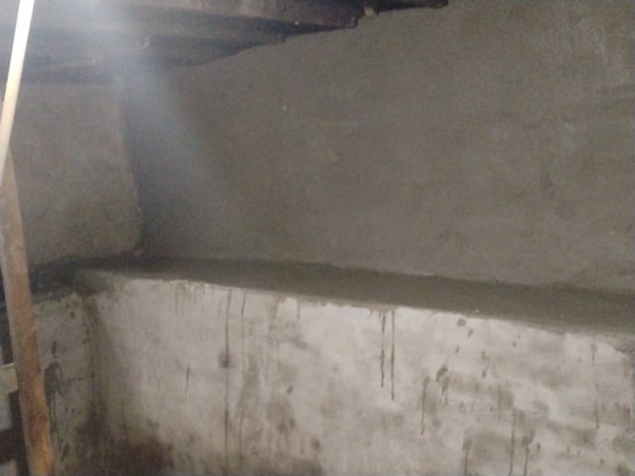 An old basement wall coated in cement, with a fresh concrete ledge along the floor