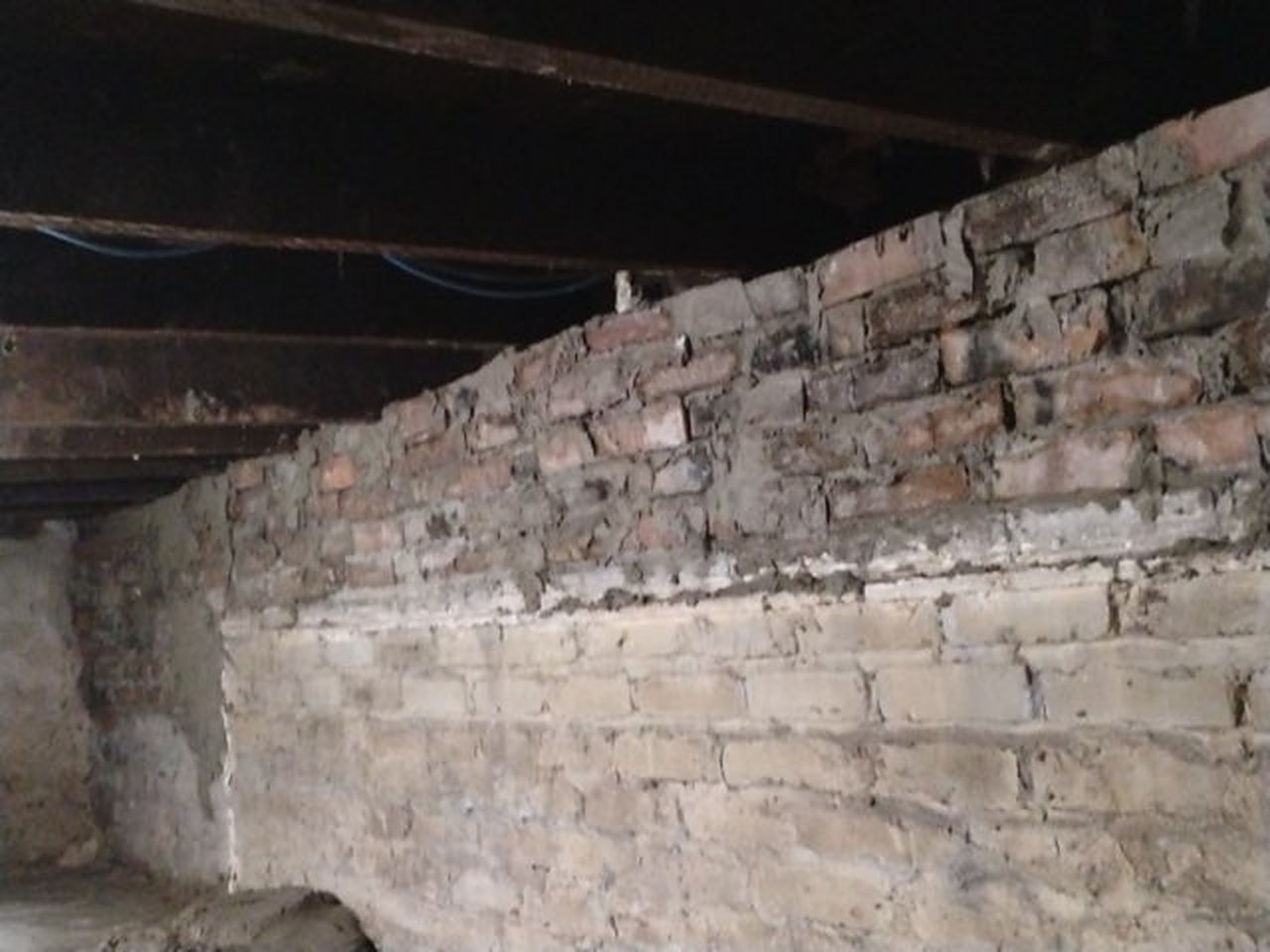 An old basement wall of rough stone on the bottom and old brick on top, before any work